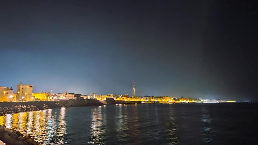 Night view of Cadiz beach with glowing buildings reflecting on the water