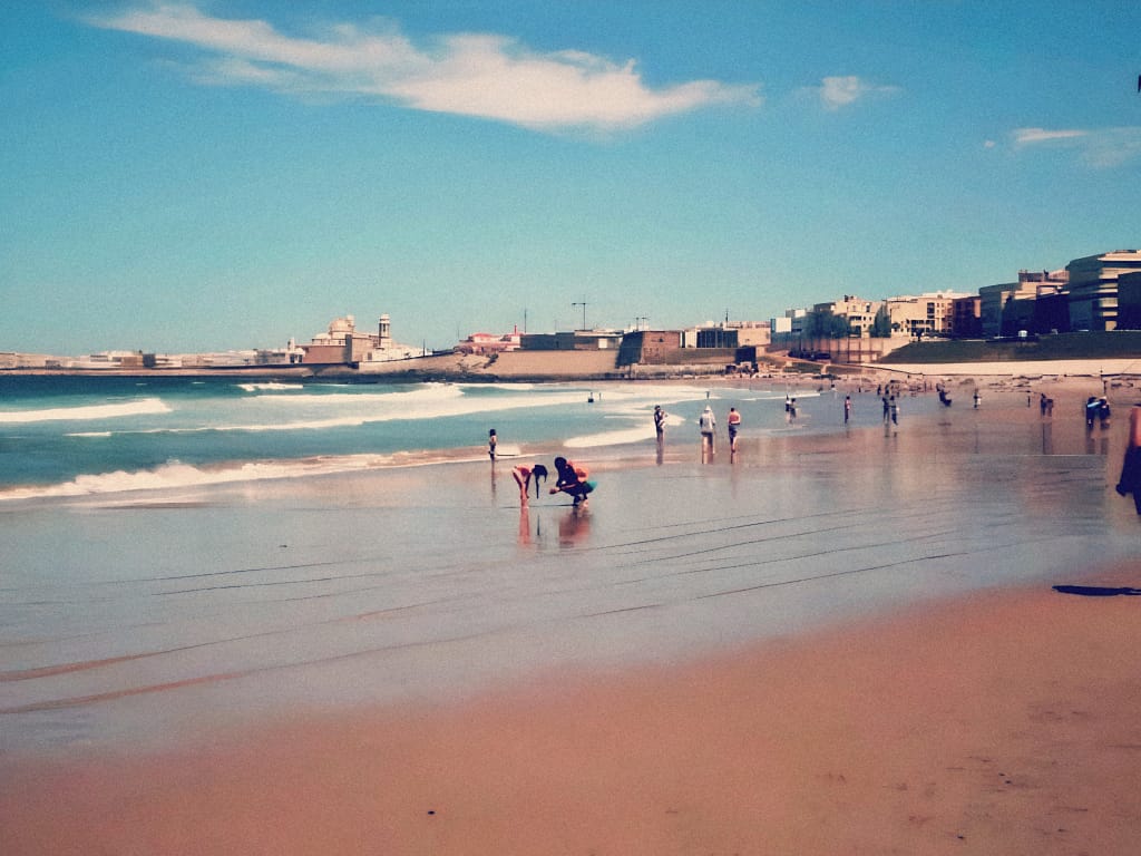 People walking along a long sandy beach in Cadiz, Spain