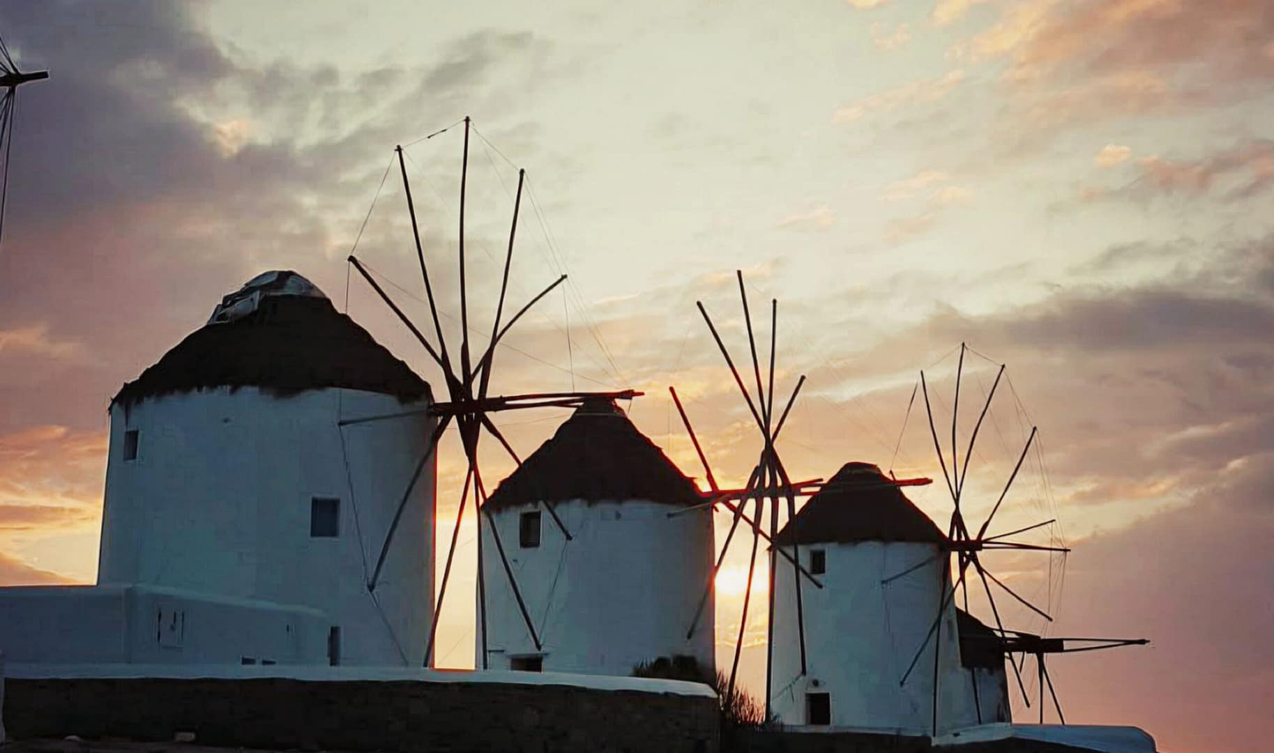 Mykonos windmills at sunset with orange sky and white silhouettes in Chora