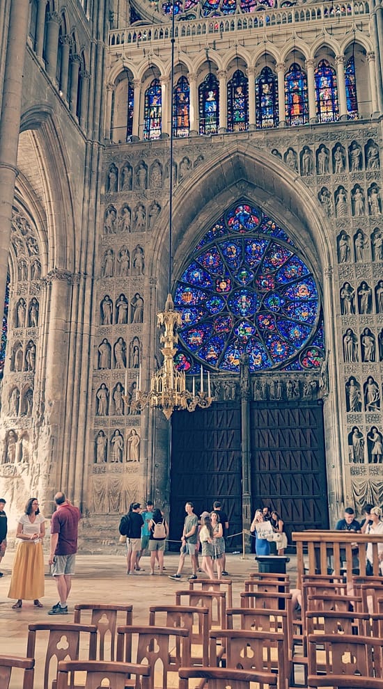 Inside Reims Cathedral showing the large stained-glass rose window and carved Gothic stonework.