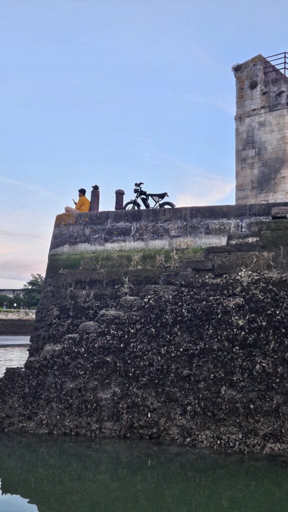 man wathcing the view from the walls of the port with his motorbike behind him