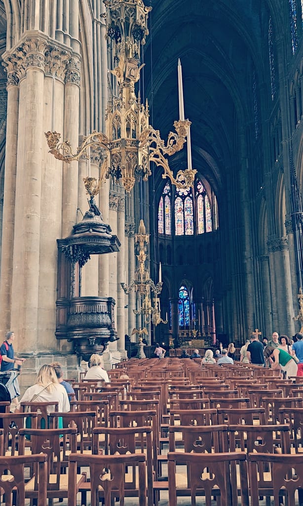 Reims Cathedral interior with long nave, ornate chandelier and stained-glass windows.