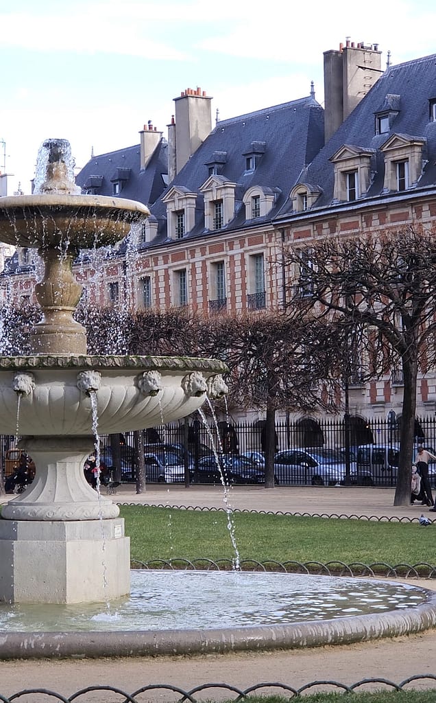 Fuente en la Place des Vosges en Le Marais, París, con edificios históricos al fondo.