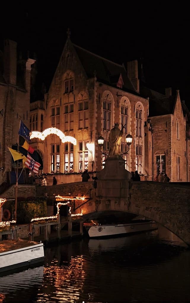 Vista nocturna del canal de Brujas decorado con luces navideñas junto al puente y edificio histórico.