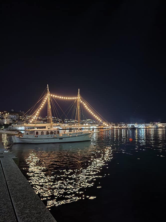 Traditional boat at night in Mykonos harbor, golden lights reflecting on the water