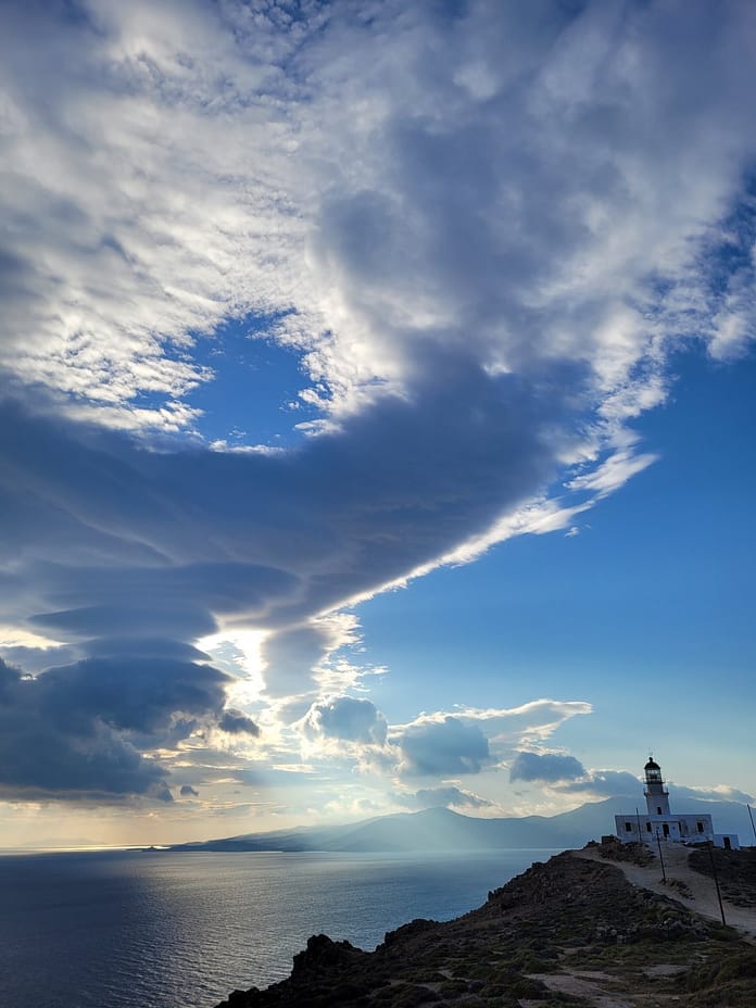 Faro de Armenistis en Mykonos con vistas panorámicas al mar Egeo y cielo dramático al atardecer